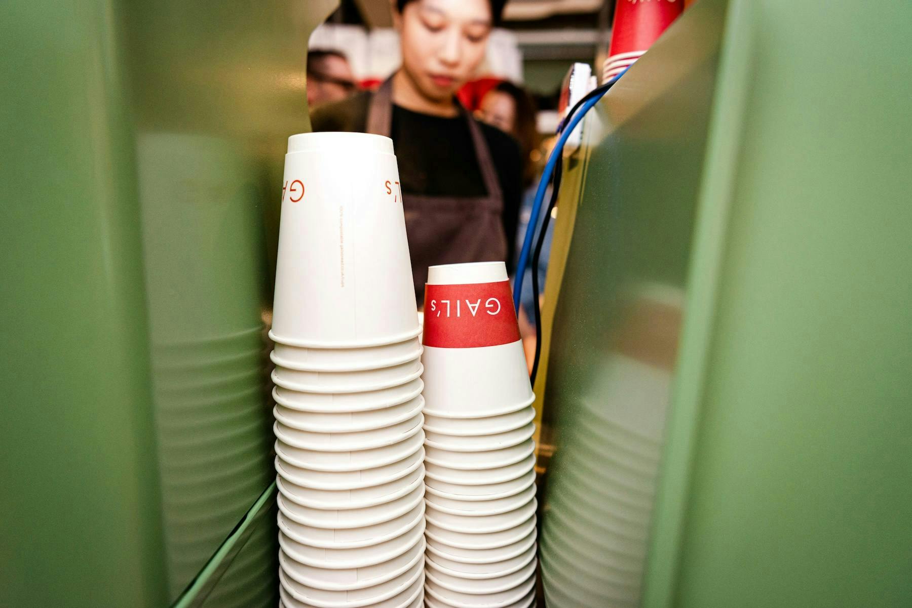 a front of house member serves coffee behind a stack of coffee cups