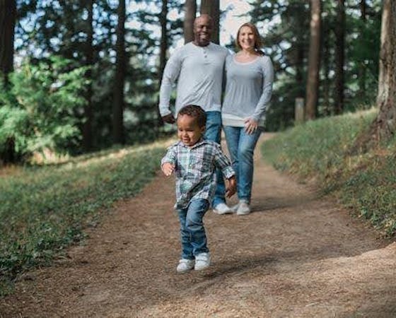 Image of a family walking in a forest with the child in the foreground.