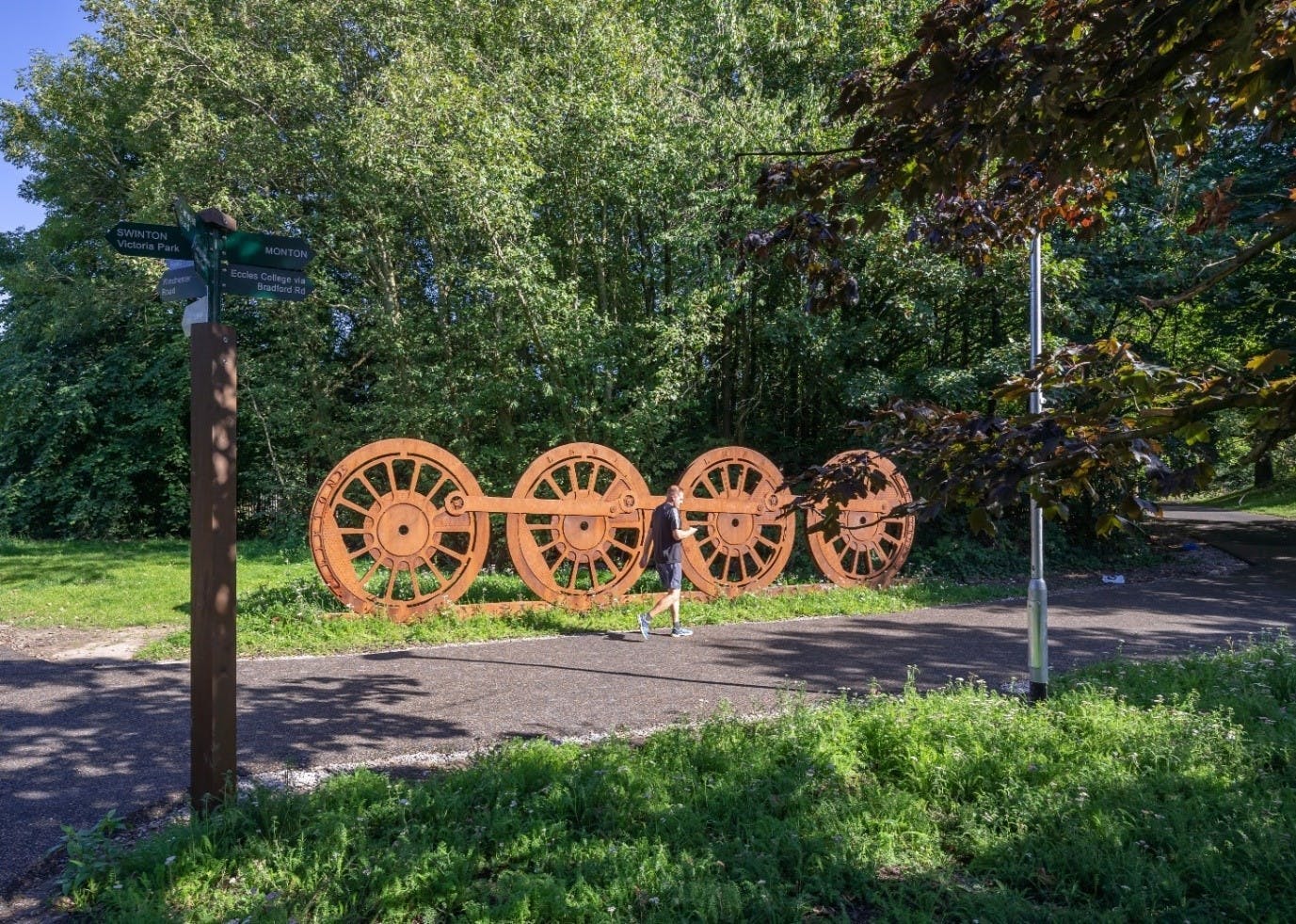 Image of a park with an old set of train wheels visible and a man running.