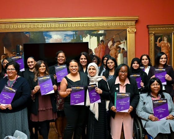 Group of women smiling and holding certificates after completing the LeadHership program, standing together in a formal setting with a classical painting in the background.