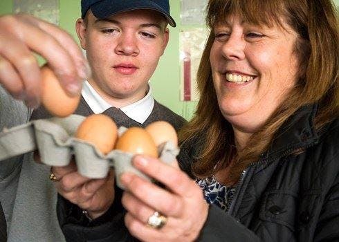 Image of a smiling woman and a young man holding a basket with eggs in it.