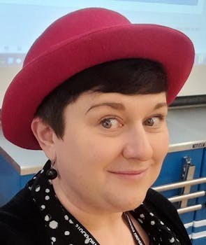 Side portrait of a lady with short hair wearing a round hat.