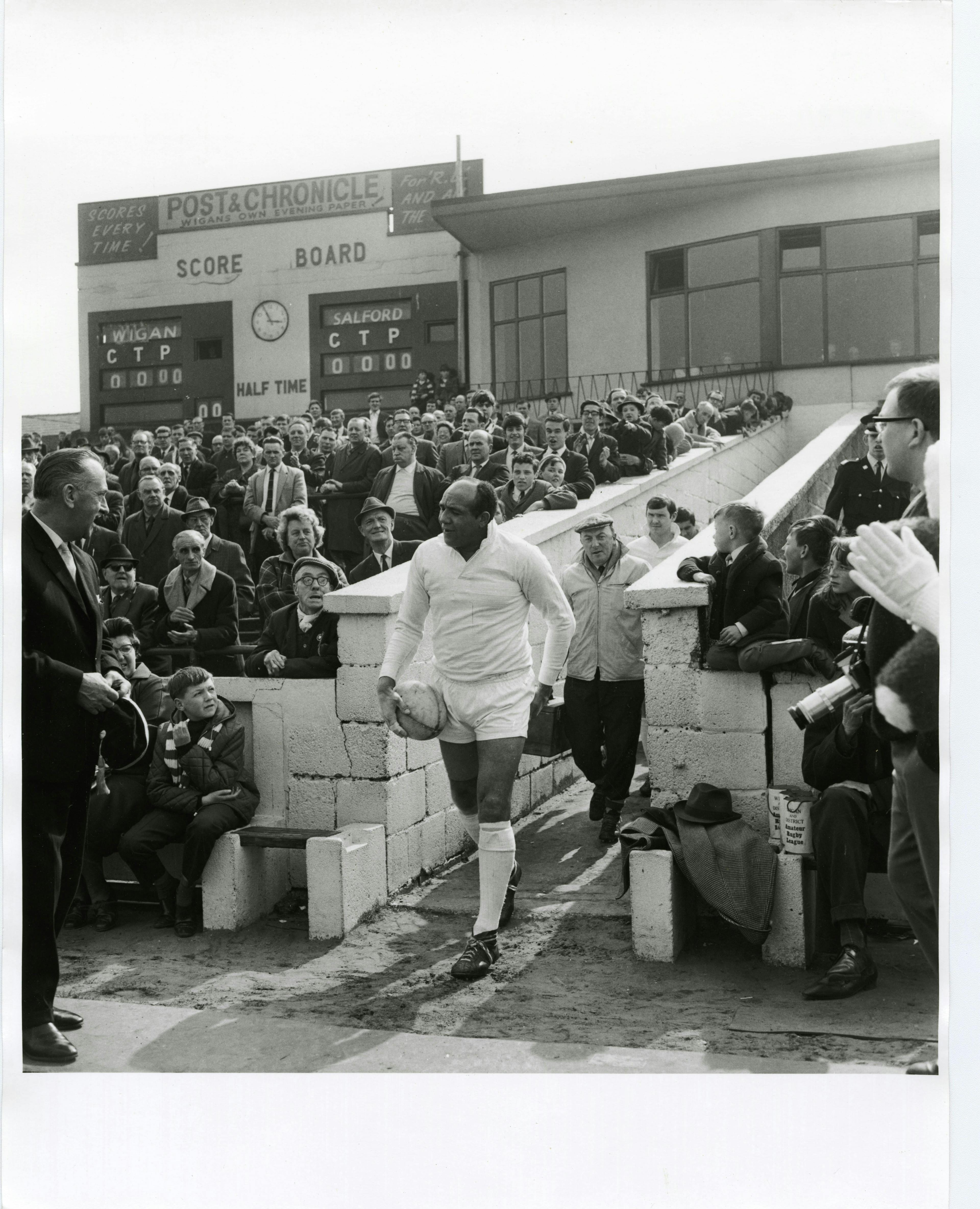 Football player Billy Boston exiting a building surrounded by fans during his last match for Wigan (Wigan vs. Salford, 1968)