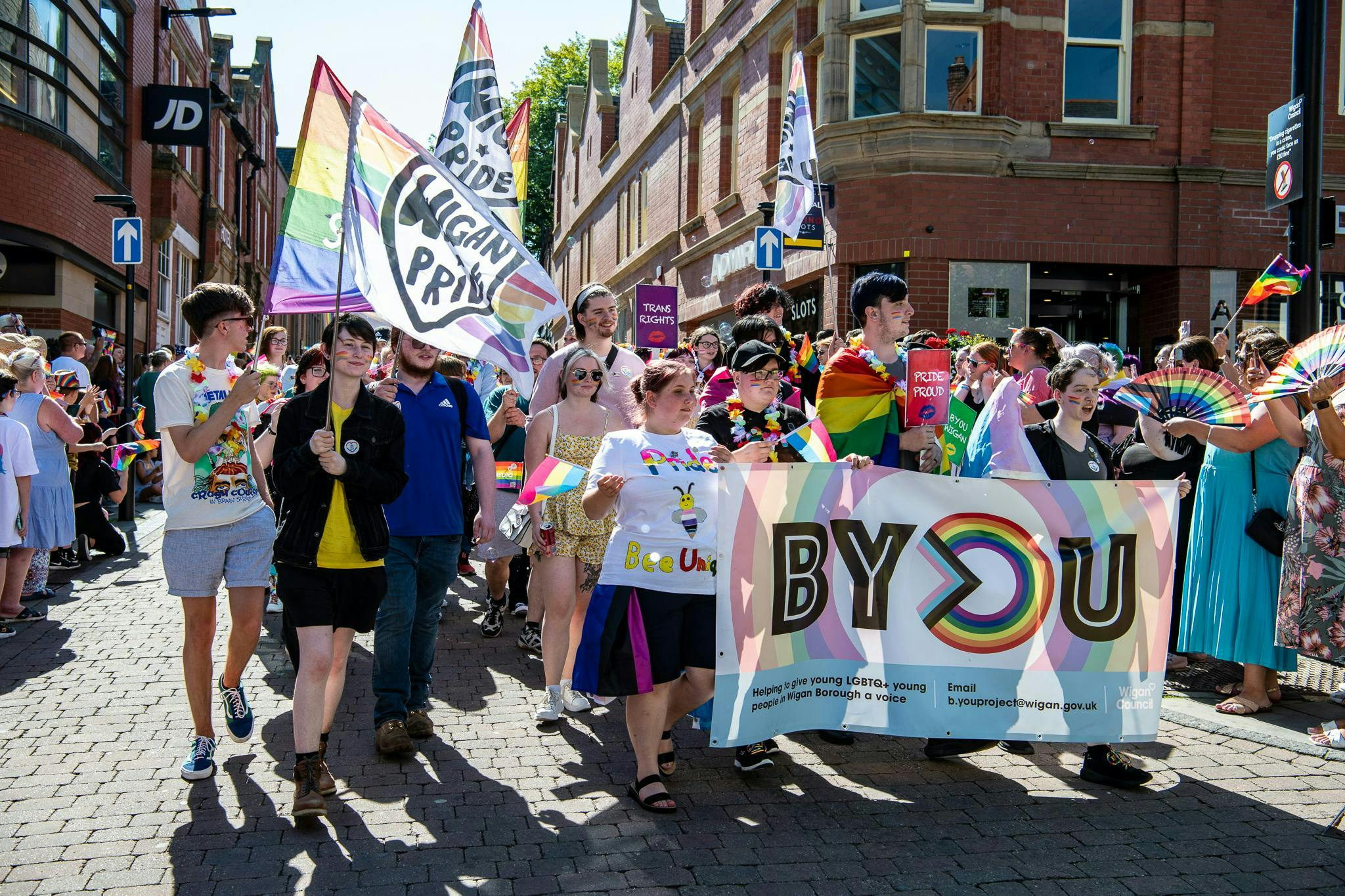 Colourful image of people holding flags marching for Wigan Pride 2022