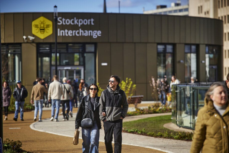 Image of Stockport Interchange building with a group of people walking in front of it, and a couple in the foreground.