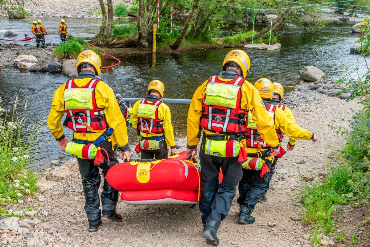 Image of five people with helmets and life jackets carrying a raft towards a river.