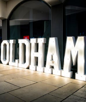 Image of a large window with a lighted letter statue spelling "Oldham" in front.