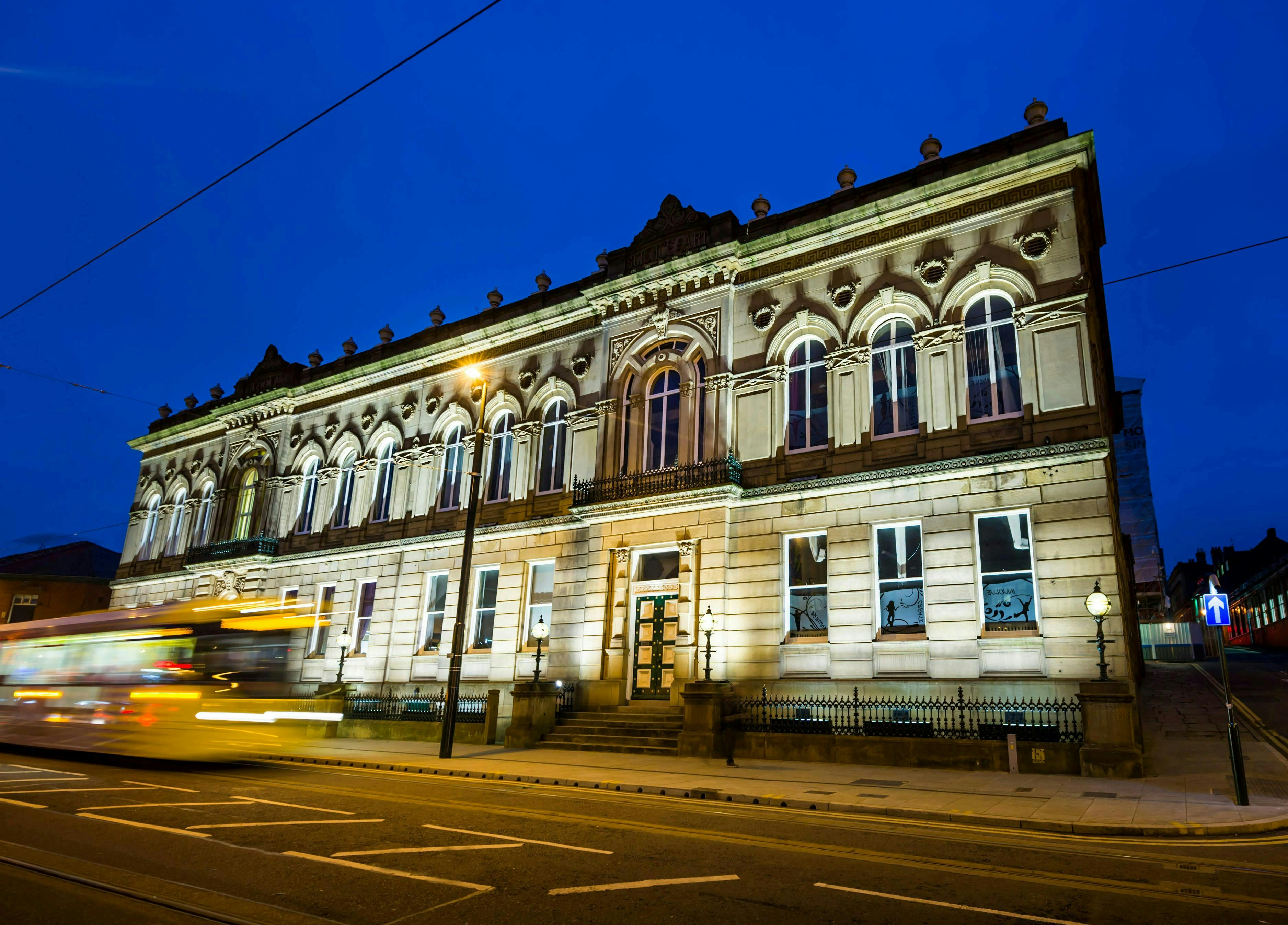 Nighttime image of a building with a tram passing in front of it.