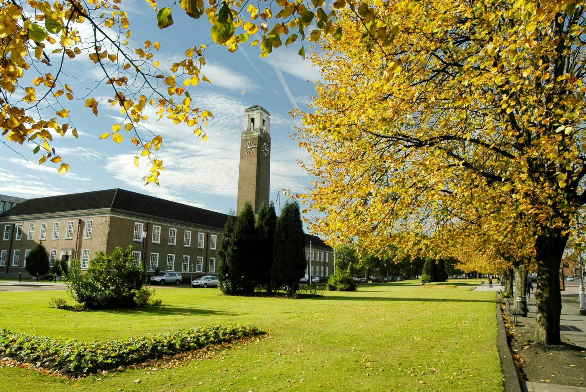Image of the Civic Center of Salford with lush green grass in the foreground and yellow trees.