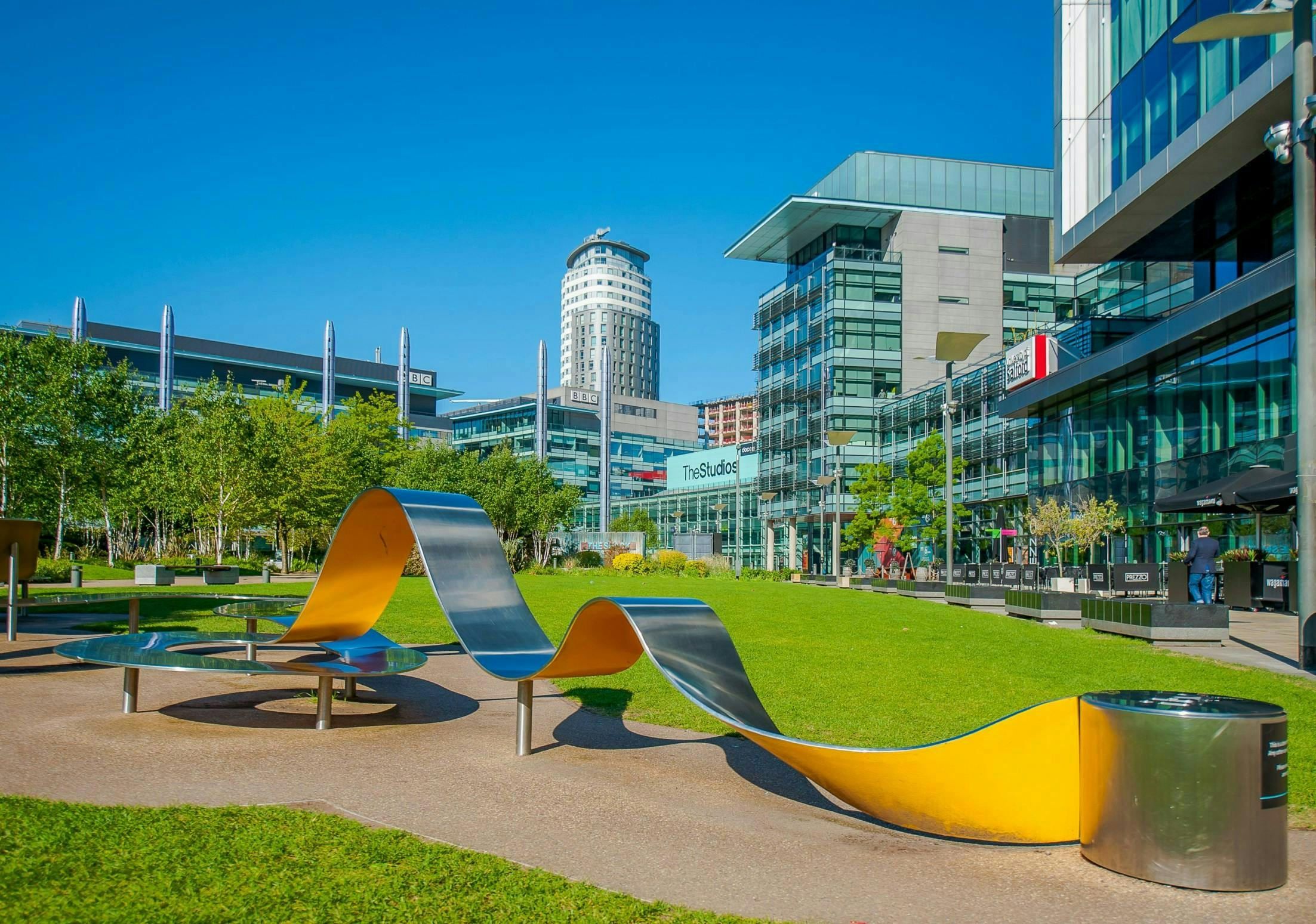 Image of a sunny day with glass buildings in the background and a metallic sculpture in the foreground.